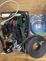 Box containing power strip, extension cord, assorted cables, Electrohome lens cleaner