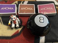 Lot overview showing Magic 8 Ball, three Anomia decks, Coca-Cola bear