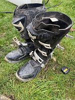 Overall view of both boots standing upright on grass showing general condition, buckles, and upper construction