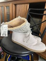 Side view of right boot with tag, showing leather upper, knit collar, fleece lining and lace detail