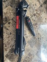 Folded Sony tripod with attached wired remote handle shown on tabletop