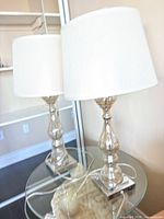 Pair of silver glass table lamps with white shades on table