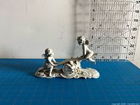 Front view of bisque cherub figurine on blue grid mat with ruler backdrop