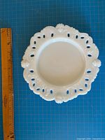 Top view showing entire dish, lace rim, cherub heads, and ruler for scale