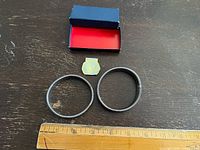 Open box showing two sleeve garters, paper seal, ruler for scale