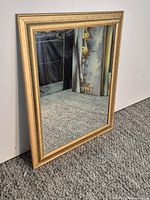 Full view of rectangular mirror with gold frame leaning against wall
