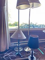 Group view of three lamps: one brass floor, one black floor, one black table with beige shade; cords visible