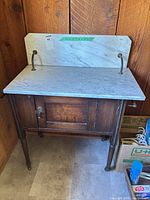 Front view of washstand showing marble top, backsplash, wood base, door, legs