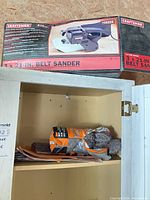 Boxed Craftsman belt sander on cabinet with abrasive bundle visible