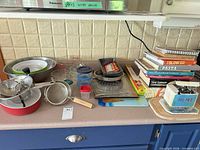 Overview of all cookware, bakeware, storage containers, utensils and cookbook stack on countertop