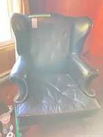 Front view of black faux leather wingback chair showing overall style, tufting and nailhead trim