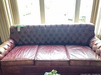 Front view of burgundy leather Chesterfield sofa with tufted back and three cushions