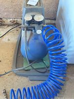 Front view of compressor showing tank, gauges, regulator and blue hose