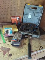 Lot overview showing drill in case, RIDGID bits, driver kit, hammer, staples and hardware