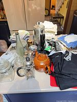 Overview of lot on countertop showing teapot, French press, percolator, jars, linens and accessories