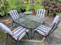 Full view of square glass table with four cushioned chairs on patio