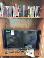 TV on shelf with remotes, manual, media above