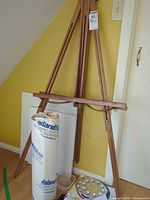 Full view of wooden tripod A-frame easel with art supplies at base
