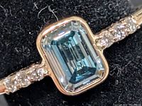 Front view of ring showing emerald-cut blue center stone and side diamonds