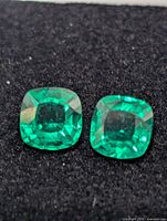 Close-up of both cushion-cut created emeralds on black background
