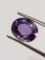 Front view of oval amethyst held by tweezers