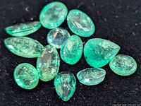 Group of 11 loose faceted emerald gemstones on black background