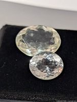 Two oval faceted pale green gemstones on black pad