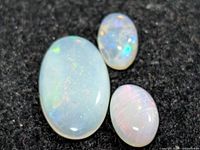 Three opal cabochons on dark background showing size and colour