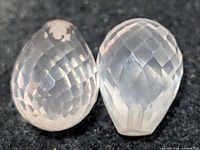 Pair of faceted teardrop rose quartz stones on dark background