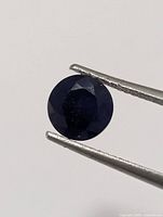 Front view of round faceted deep blue sapphire held by tweezers