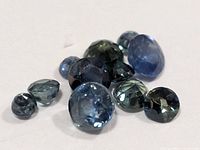 Group of loose faceted sapphires on white surface showing size and color range