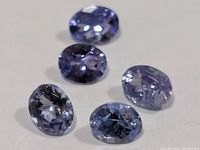 Five oval faceted violet-blue tanzanite gemstones on neutral background