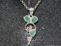 Pendant close-up showing emerald stones and clear accents