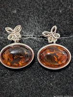Front view of both sterling silver amber earrings on black surface