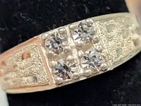 Front view of silver ring showing four clear stones and textured shoulders