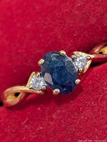 Front view of silver ring with oval blue sapphire and two clear accent stones on red background