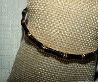 Full view of bangle on display form showing black enamel and gold-tone bamboo accents
