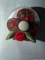 Front view showing full brooch design with plaid petals, white centre, green leaves and red rose