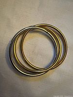 Three interlocked gold-tone metal bangles on fabric background