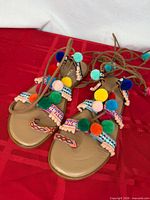 Top view pair of tan gladiator sandals with multicolor pom poms