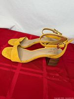 Side view of both yellow suede sandals showing ankle straps and wedge heels
