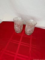 Pair of clear glass snowflake tealight holders on red cloth