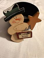 Front view of wooden snowman brooch displaying star and "Let it Glow" sign