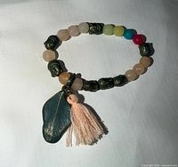 Top view of bracelet showing multicolor beads, metal accents, green stone charm and tassel