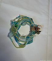 Overall view of coiled green and blue beaded bracelet with shell and fish charm