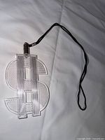Front view of clear plastic dollar sign pendant with black cord