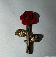 Front view of gold-tone stem and red enamel rose brooch