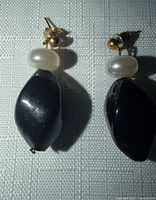 Front view of earrings showing white and black pearls and gold posts