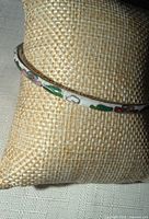 Side view of white cloisonné enamel bangle on cushion