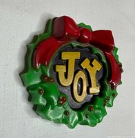 Front angled view of plastic JOY wreath brooch